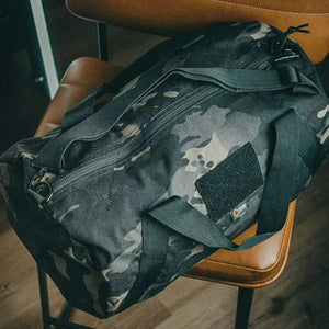 Multicam barrel duffle bag with black straps and zipper.