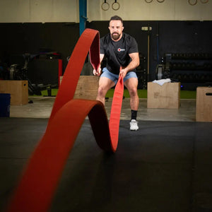 Man using a red battle rope in a gym