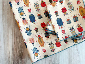 Cream cotton napkins with colorful beetle print and blue zig-zag trim, set of four.