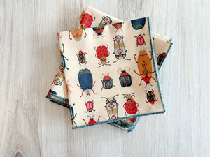 Cream cotton cloth napkins with a colorful beetle print, set of four.