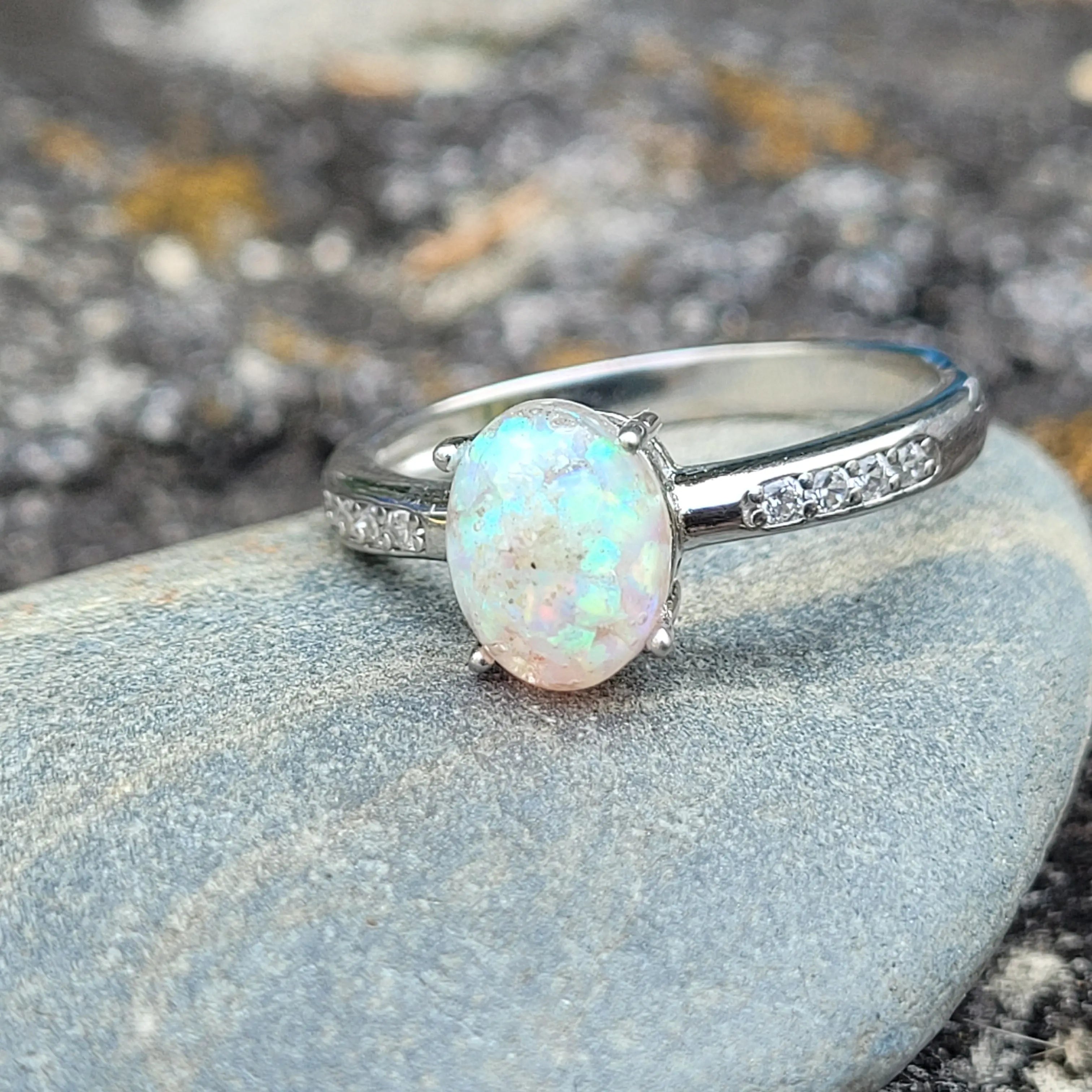 Opal ring in sterling silver with cubic zirconia accents resting on a gray stone.