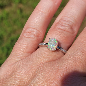 Opal Ring: A close-up of a hand wearing a sterling silver ring with an oval opal and cubic zirconia accents, set against a green background.