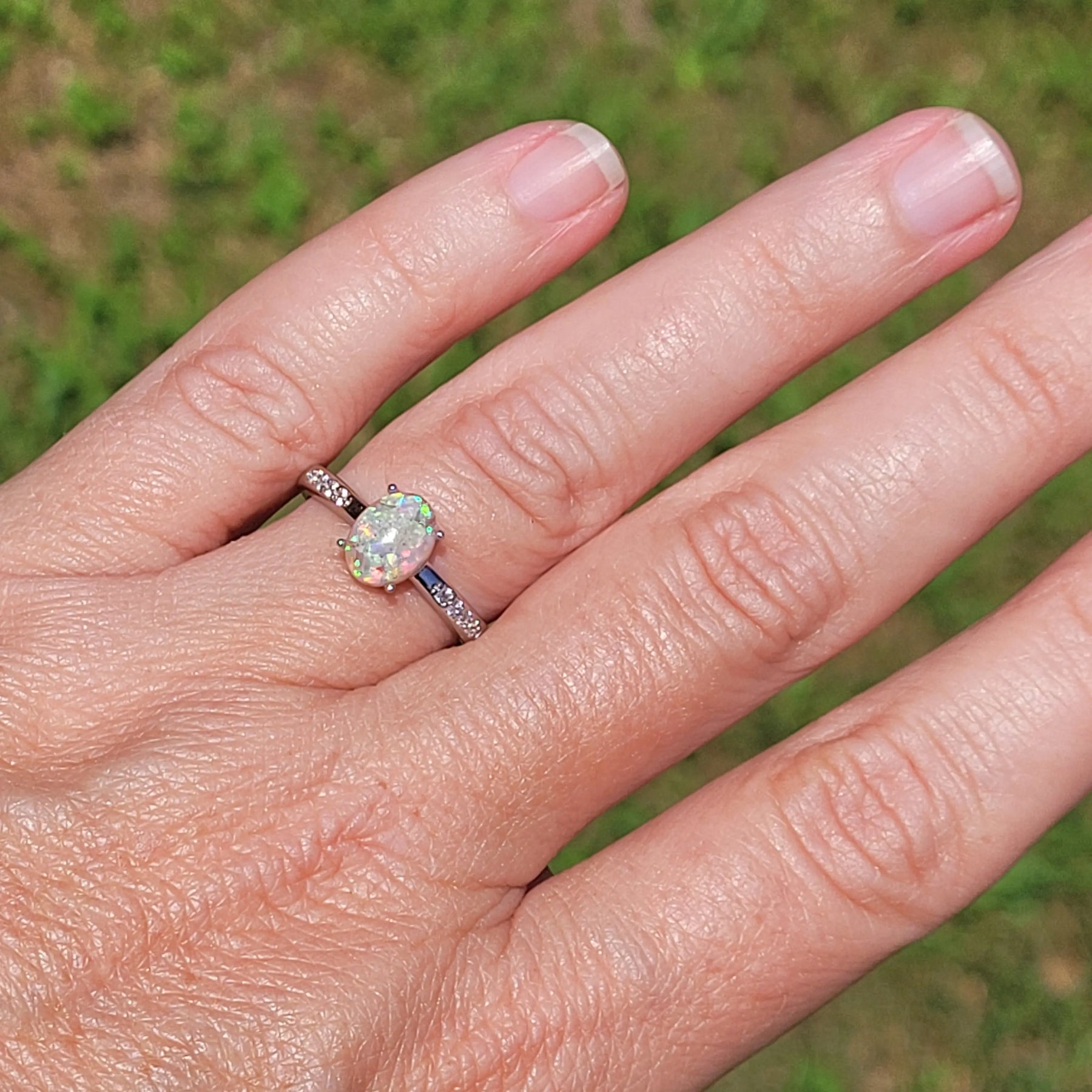 Opal ring on finger: .925 sterling silver with oval opal stone and cubic zirconia accents, set against an outdoor background.