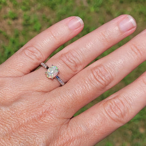 Opal ring on finger: .925 sterling silver with oval opal stone and cubic zirconia accents, set against an outdoor background.