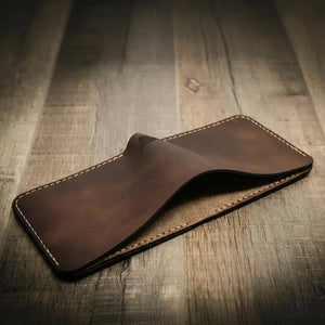 Brown leather bifold wallet with stitched edges on a wooden surface.
