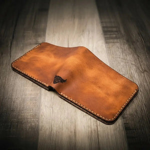 Brown leather bifold wallet with stamped bull logo on wooden surface.
