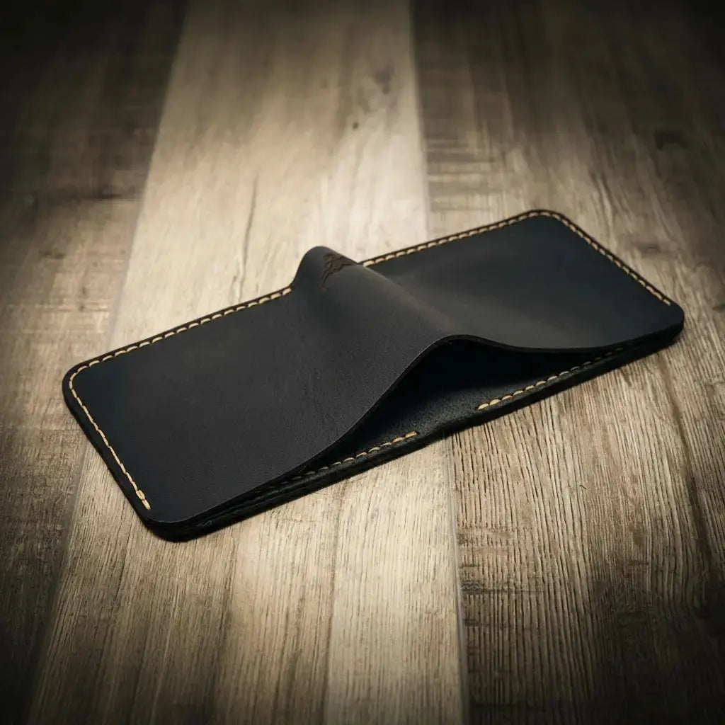 Black leather bifold wallet with tan contrast stitching on a wooden background.