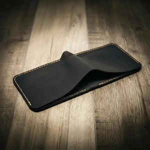 Black leather bifold wallet with tan contrast stitching on a wooden background.