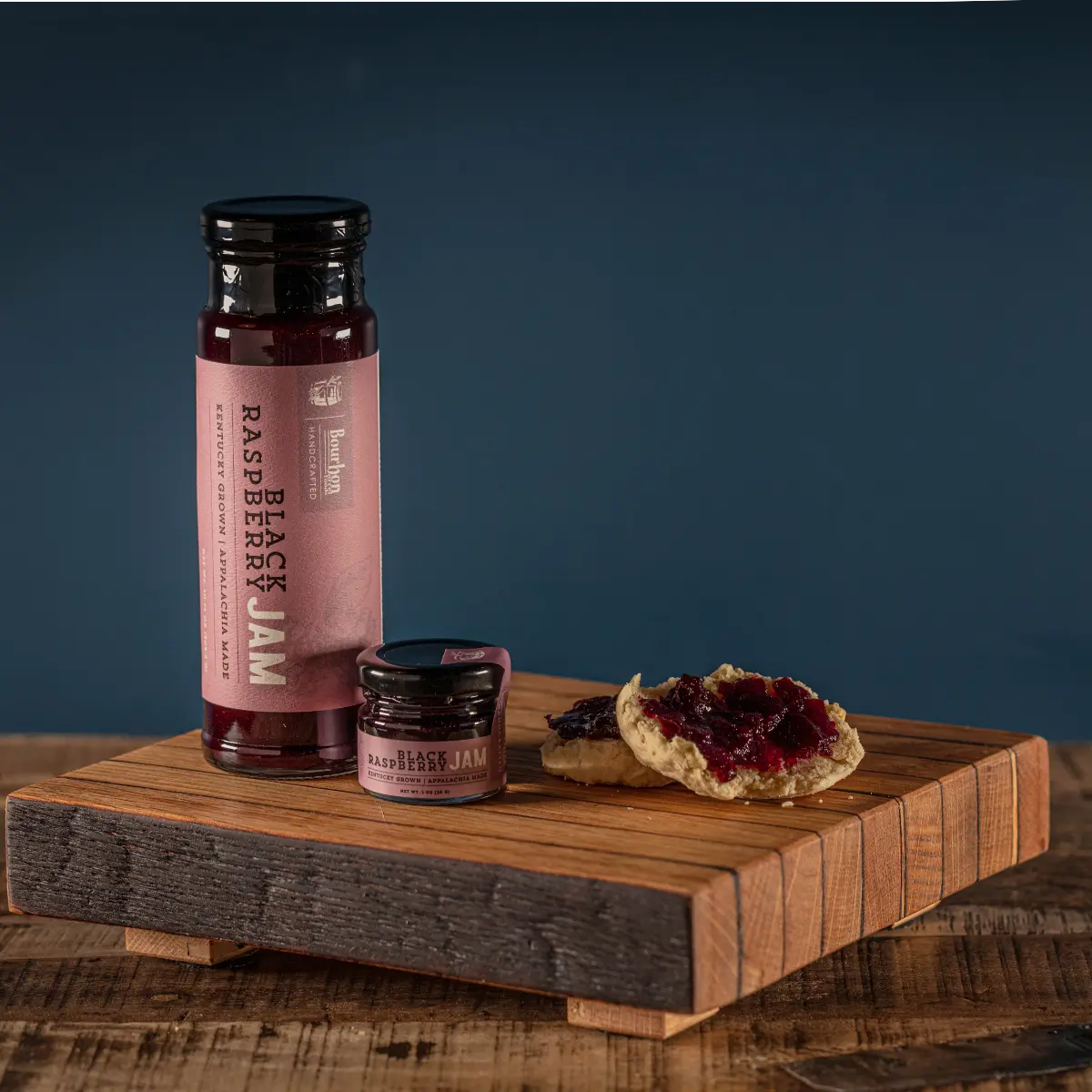 Black Raspberry Jam in jars and spread on biscuits on a wooden board.