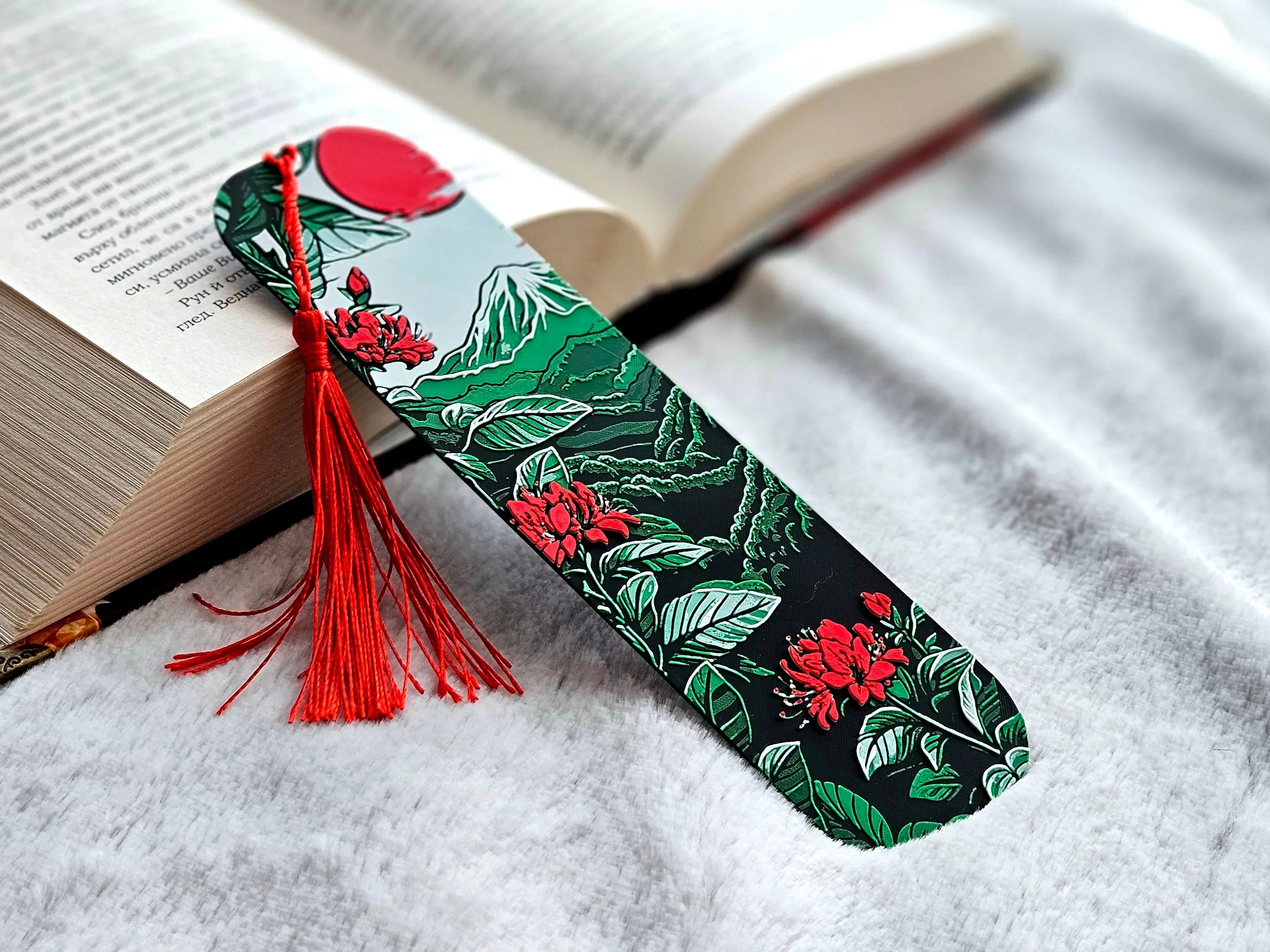 Bookmark with Mount Fuji, red sun, blossoms, and red tassel in a book.
