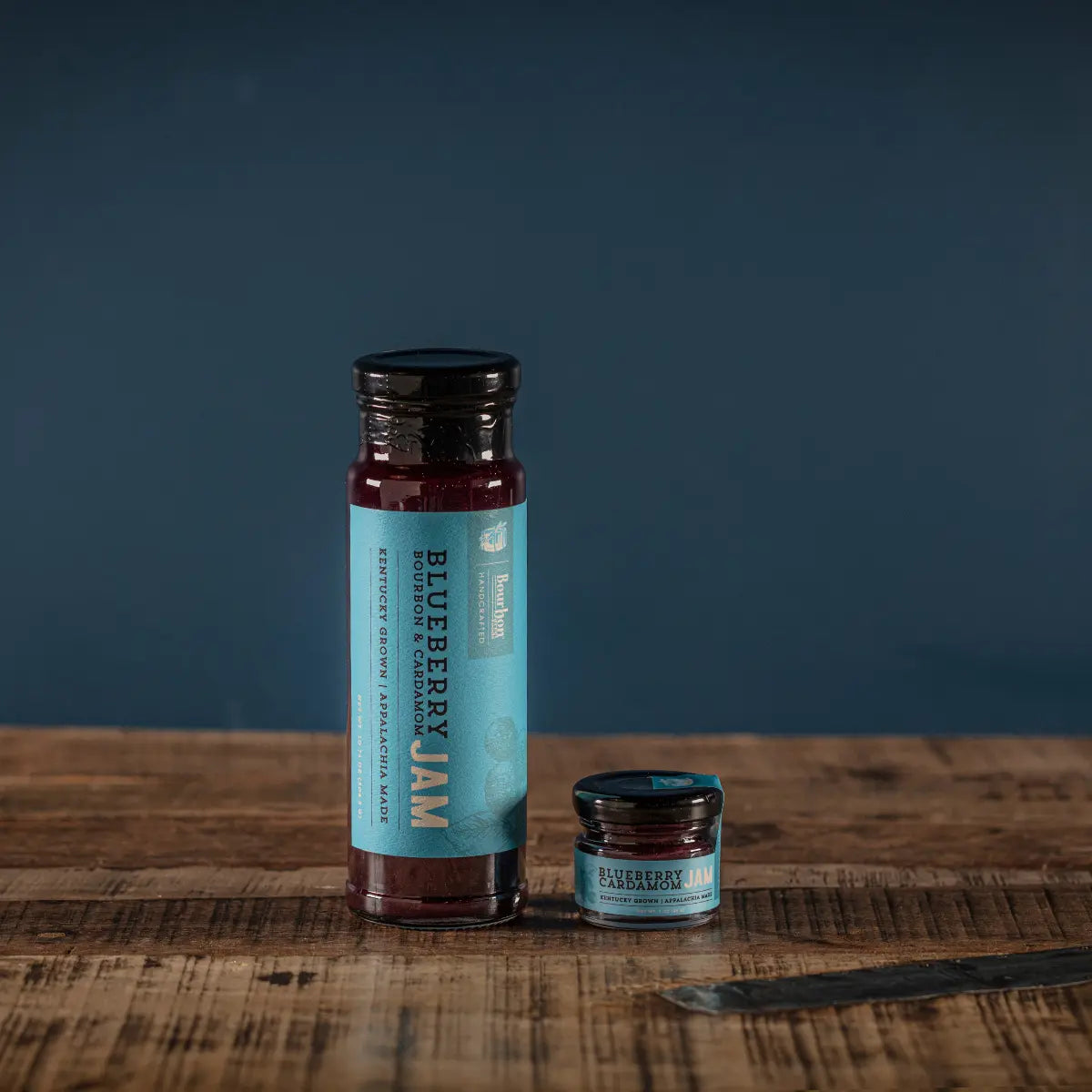Blueberry Bourbon Cardamom Jam in two glass jars on a wooden table.