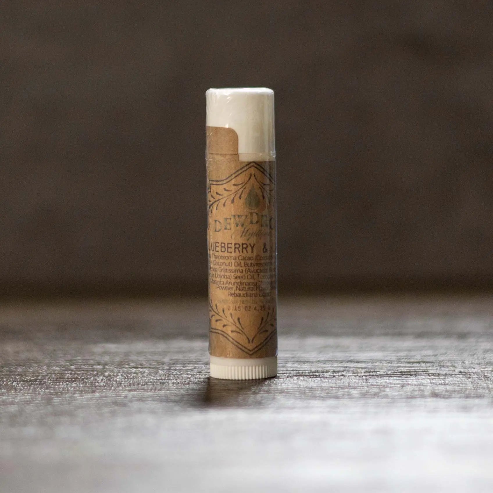 DewDrop blueberry and lemon lip balm in kraft paper tube with white cap and twist bottom on wood surface.