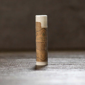 DewDrop blueberry and lemon lip balm in kraft paper tube with white cap and twist bottom on wood surface.