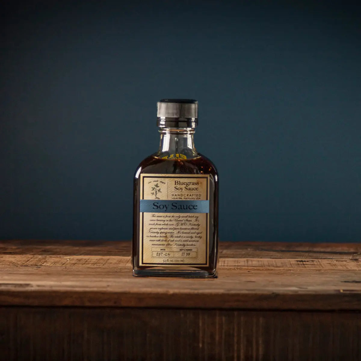 Bottle of Bluegrass Soy Sauce with a dark liquid on a wooden surface.