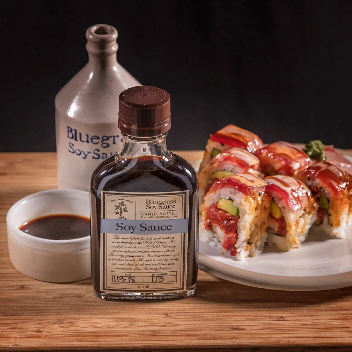 Bluegrass Soy Sauce bottle with sushi and a small dish of soy sauce on a wooden surface.