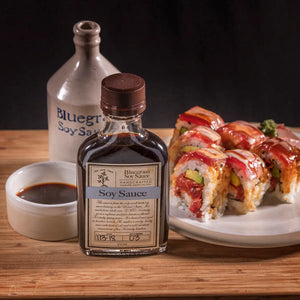 Bluegrass Soy Sauce bottle with sushi and a small dish of soy sauce on a wooden surface.
