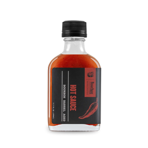 Bourbon Barrel Aged Hot Sauce in a clear glass bottle with a black cap and label.