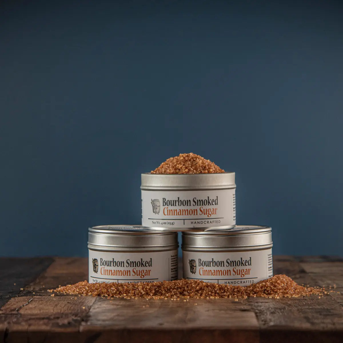 Stacked tins of Bourbon Smoked Cinnamon Sugar with raw sugar on wood