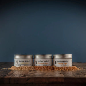 Three tins of bourbon smoked sugar: Orange, Vanilla, and Cinnamon, on a wooden surface.