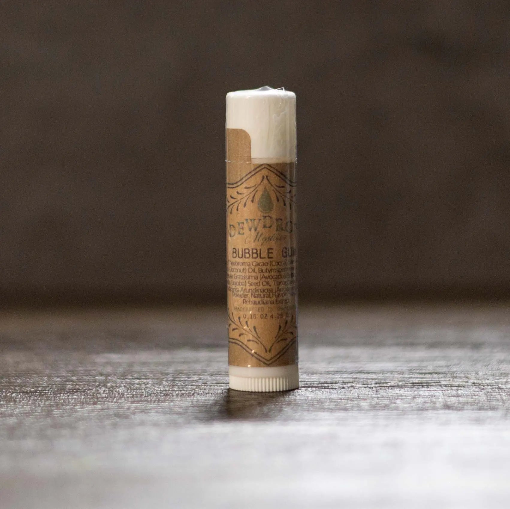 Dewdrop Bubble Gum lip balm tube with decorative label on a wood surface.