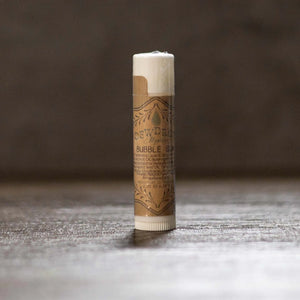 Dewdrop Bubble Gum lip balm tube with decorative label on a wood surface.