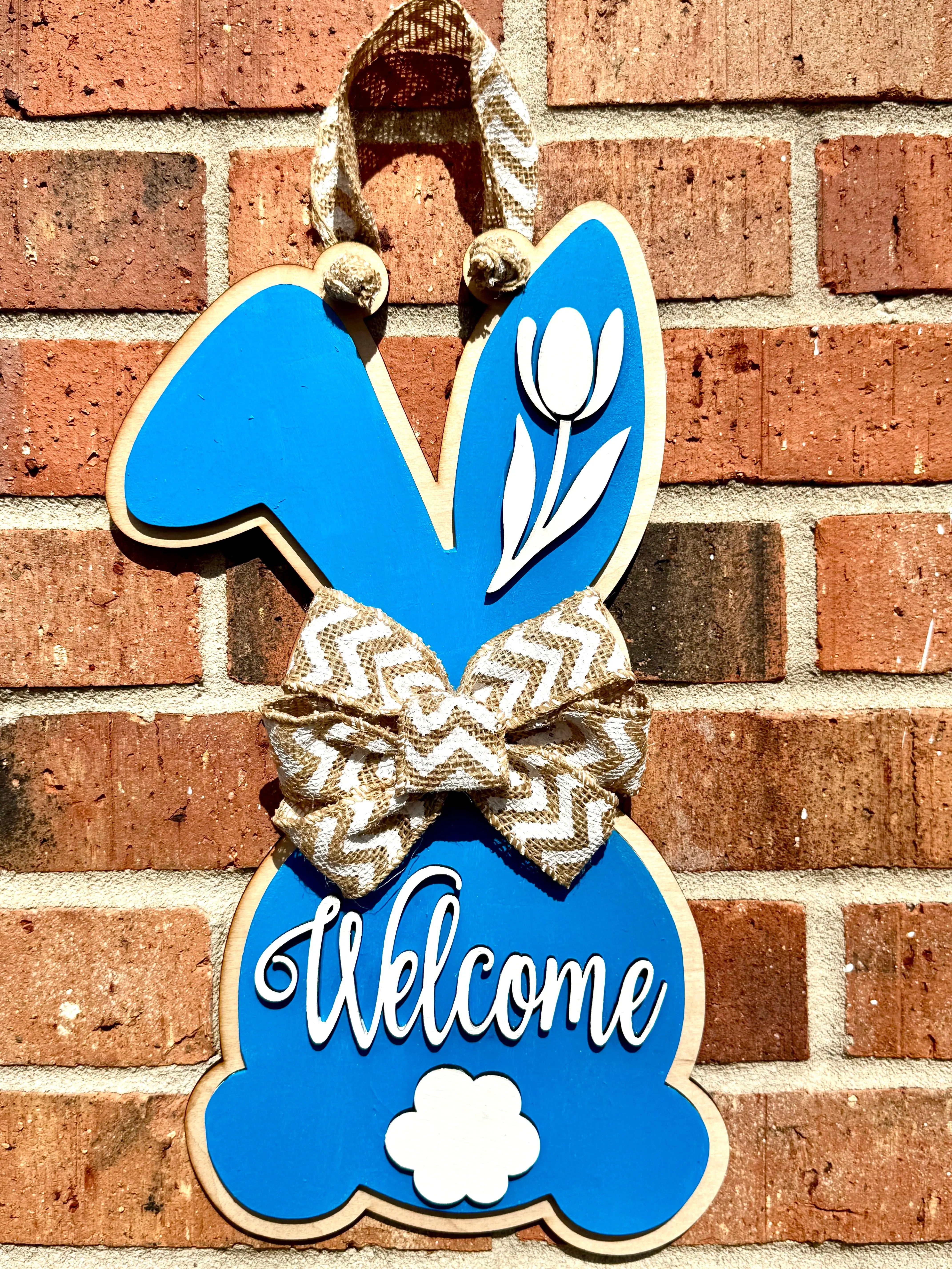 Blue wooden bunny door hanger with white tulip and "Welcome" text.