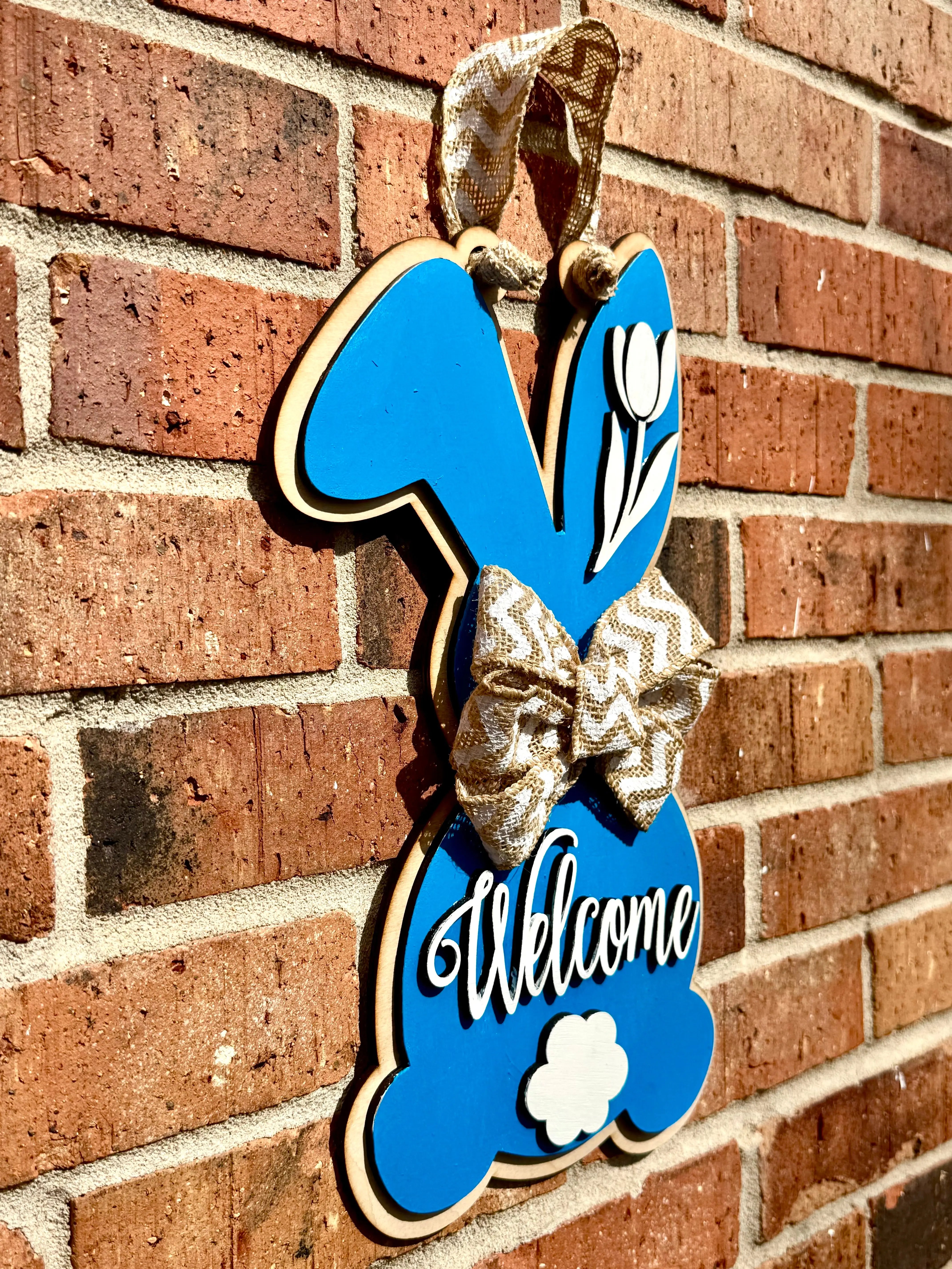 Blue bunny door hanger with "Welcome" text and a burlap bow on brick.