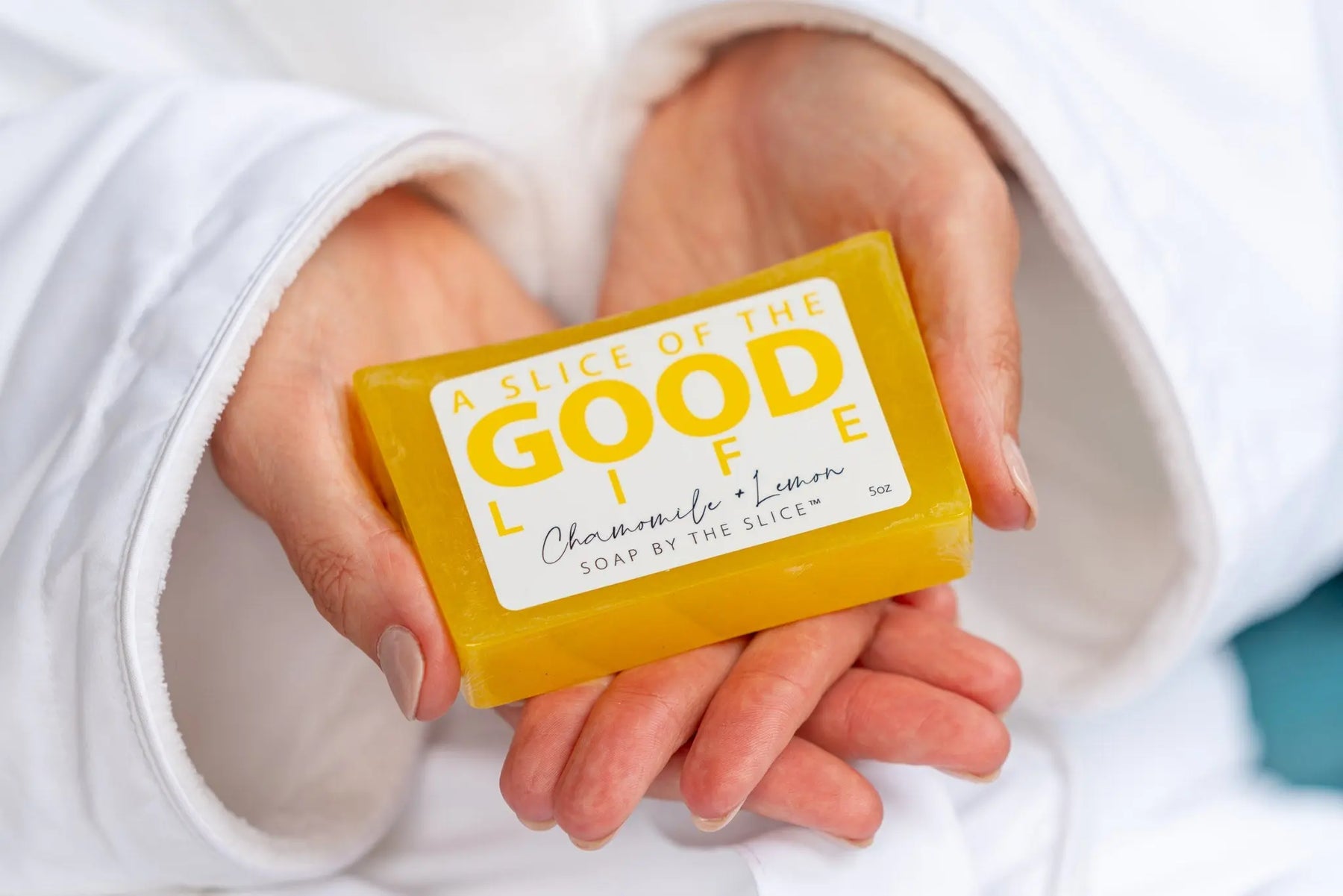 Yellow soap bar with "Good Life" label held by hands in a white robe.