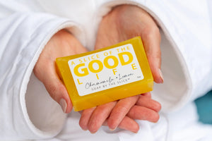 Yellow soap bar with "Good Life" label held by hands in a white robe.