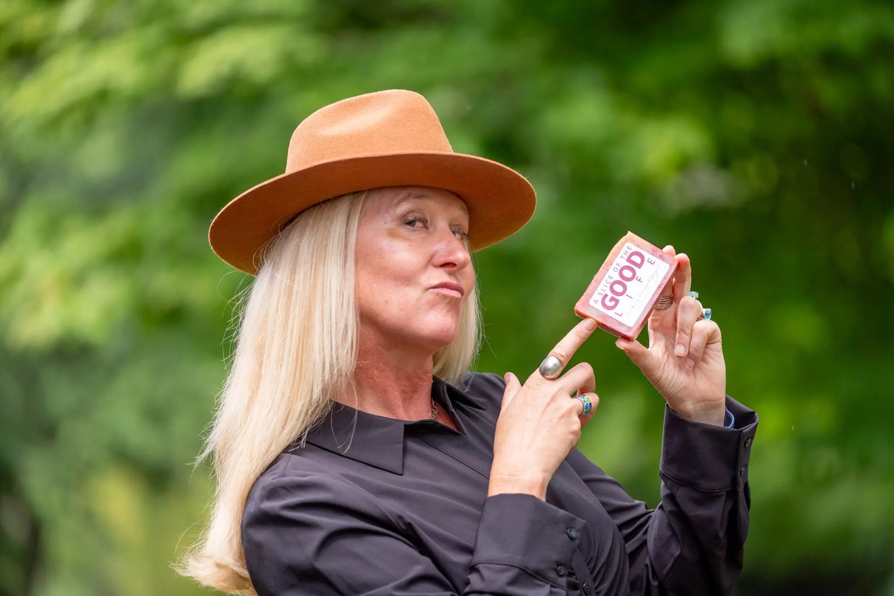 Woman in fedora hat holding a bar of Cranberry Orange Poppy Seed Soap.
