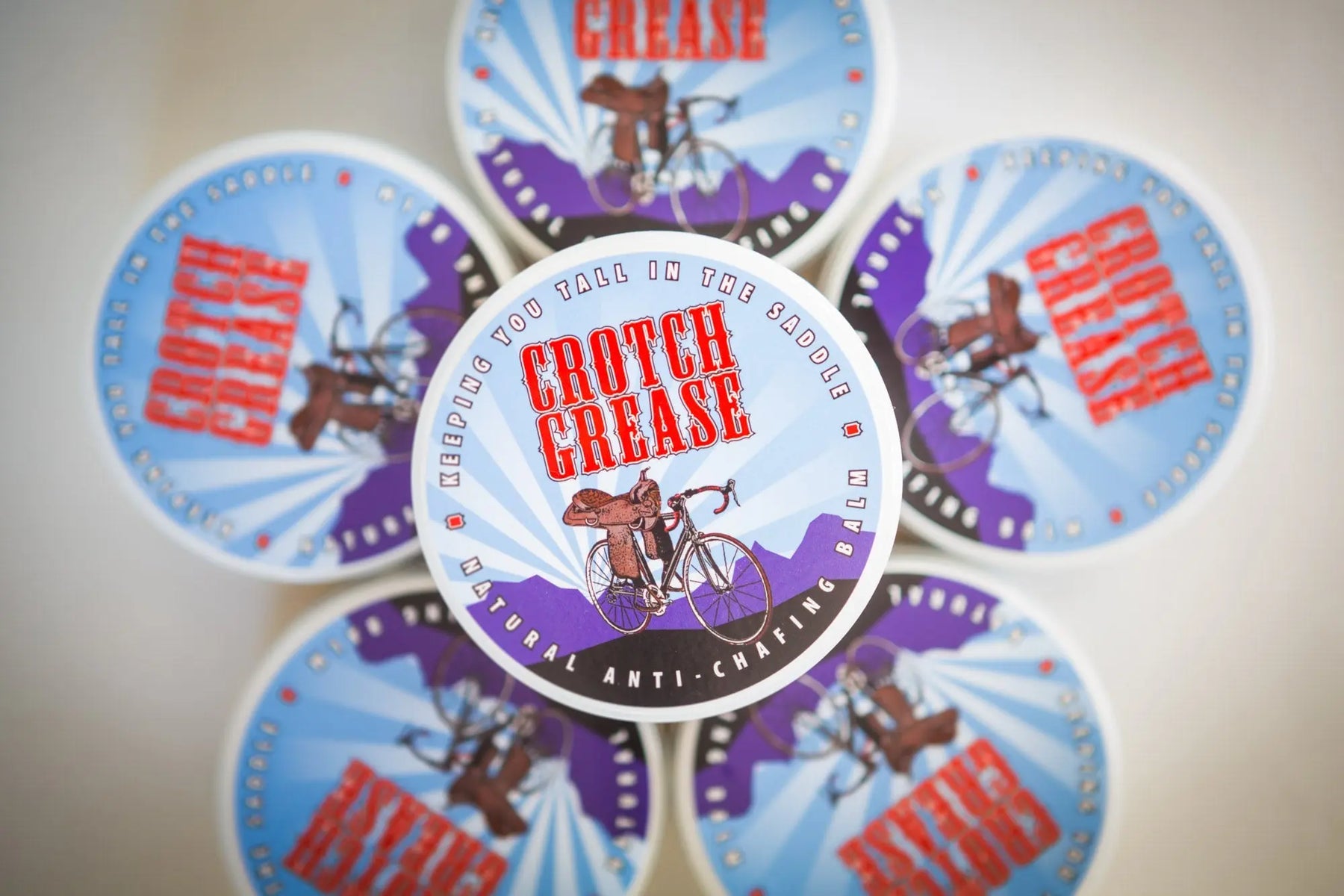 Multiple containers of Crotch Grease natural anti-chafing balm arranged in a circular pattern.