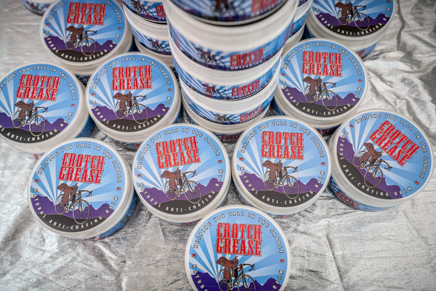 Round containers of Crotch Grease anti-chafing balm with bicycle and saddle graphics.