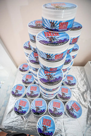 Stack of Crotch Grease unscented anti-chafing balm tubs with cyclist graphics.