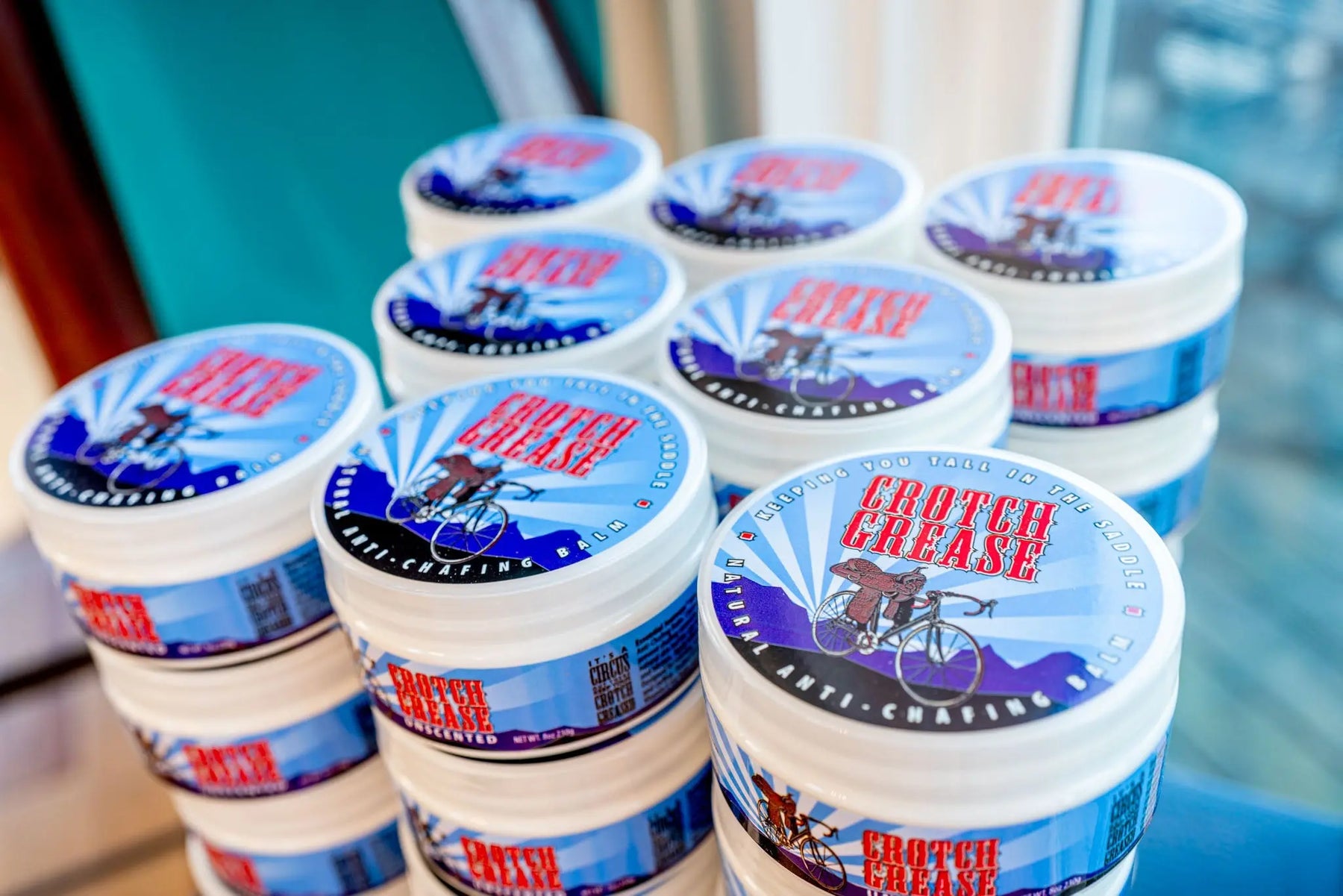 Stack of Crotch Grease anti-chafing balm tubs with blue and red labels.