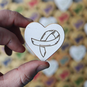 White heart token with engraved cancer awareness ribbon symbol held by fingers.