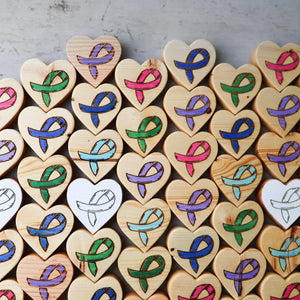 Wooden heart shapes with colored cancer awareness ribbons in rows.