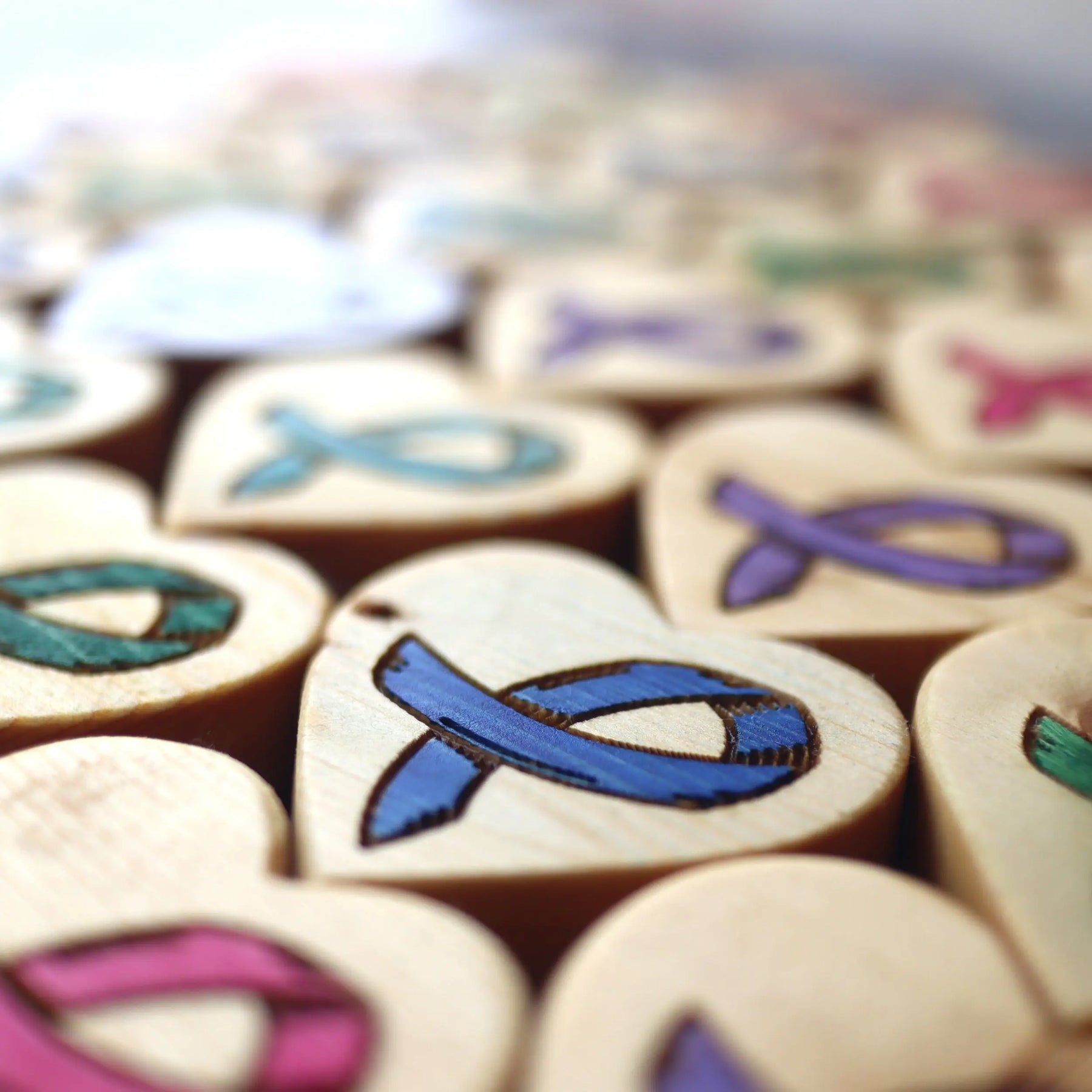 Wooden hearts engraved with colorful cancer awareness ribbons in a close-up view.