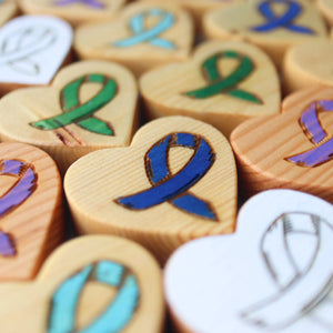 Wooden heart shapes engraved with colorful cancer awareness ribbons.