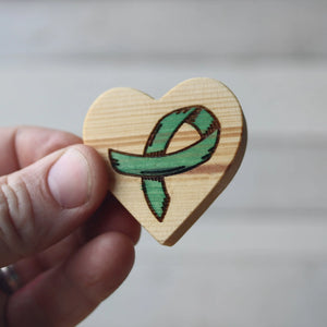 Wooden heart-shaped cancer awareness ribbon charm held in a hand