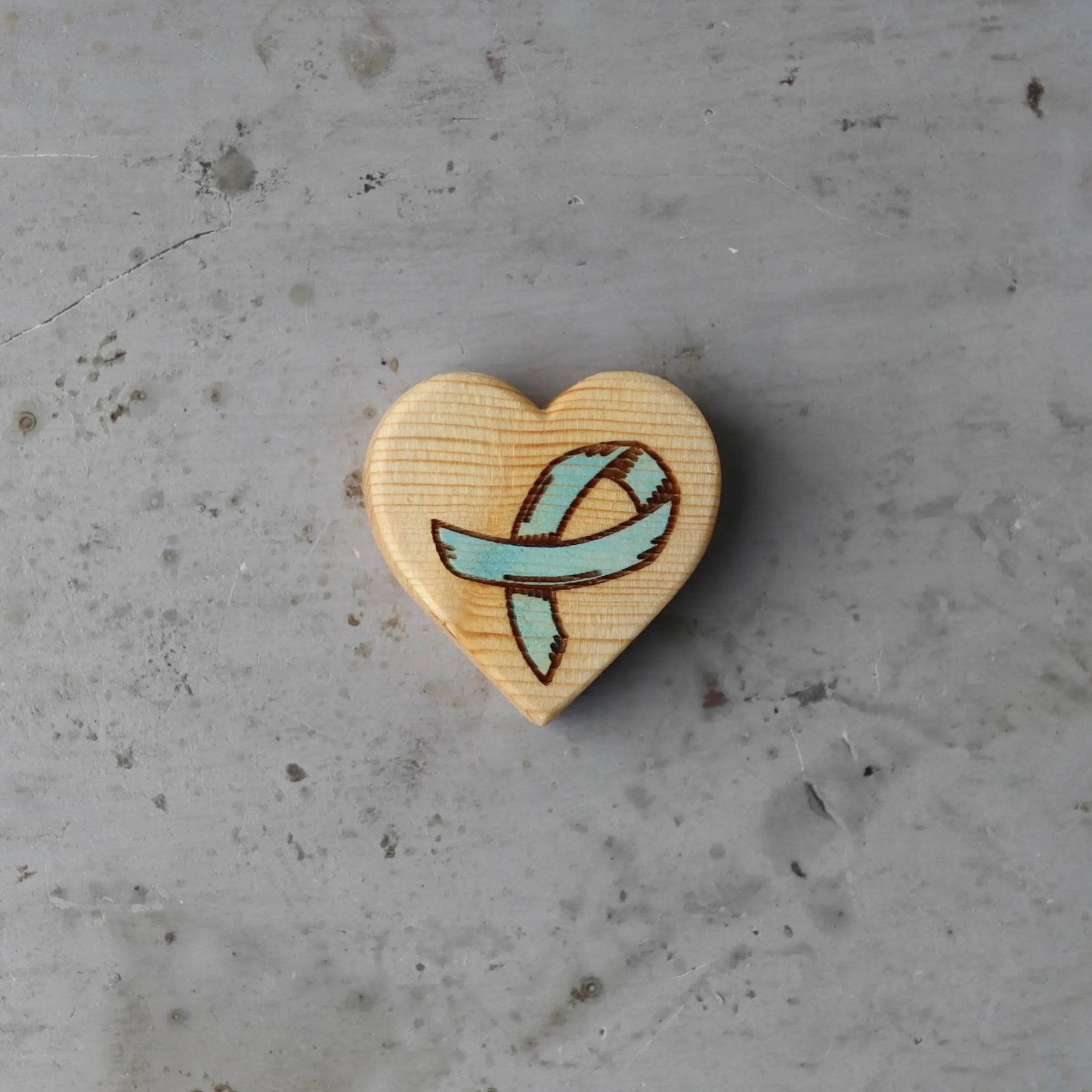 Wooden heart with a teal cancer awareness ribbon engraving.