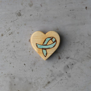 Wooden heart with a teal cancer awareness ribbon engraving.