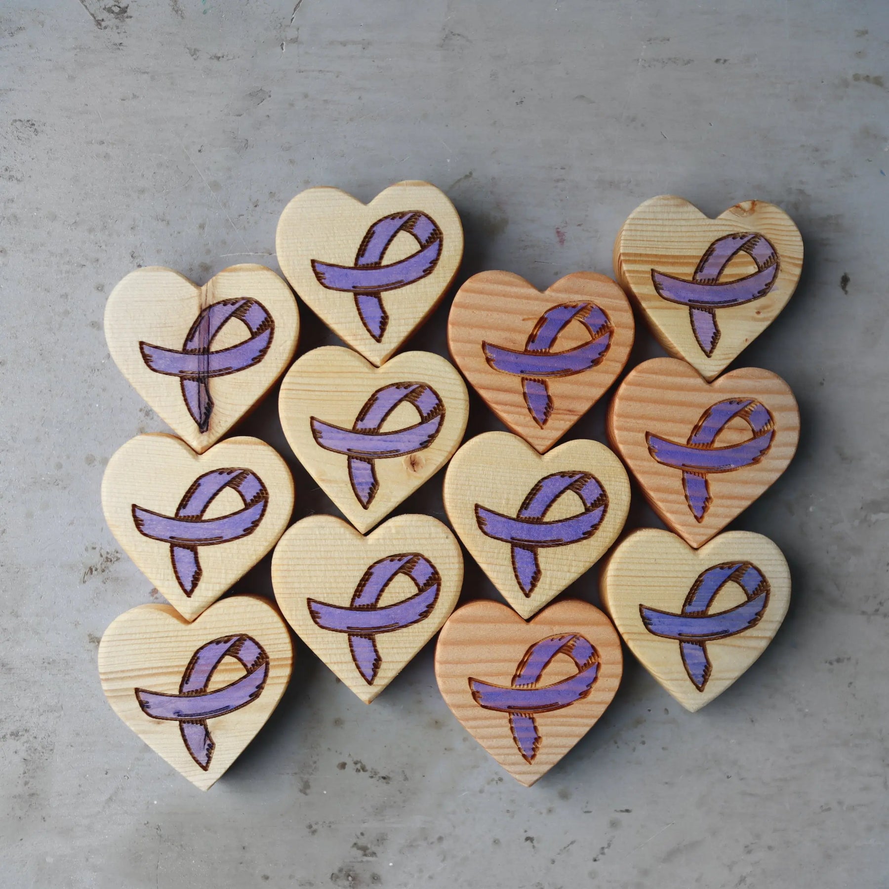 Wooden heart shapes with purple awareness ribbons etched on a grey surface.