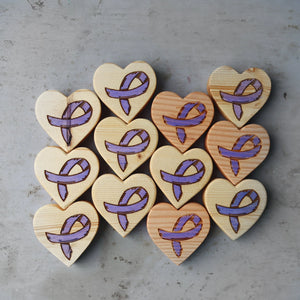 Wooden heart shapes with purple awareness ribbons etched on a grey surface.