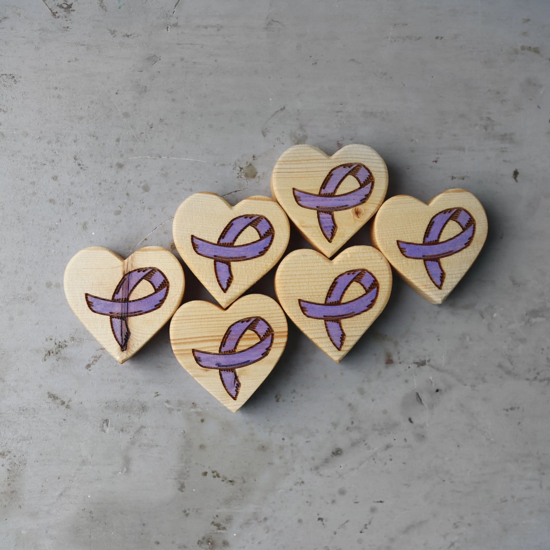 Wooden hearts with purple cancer awareness ribbons on a gray background.