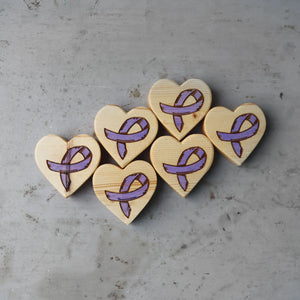 Wooden hearts with purple cancer awareness ribbons on a gray background.