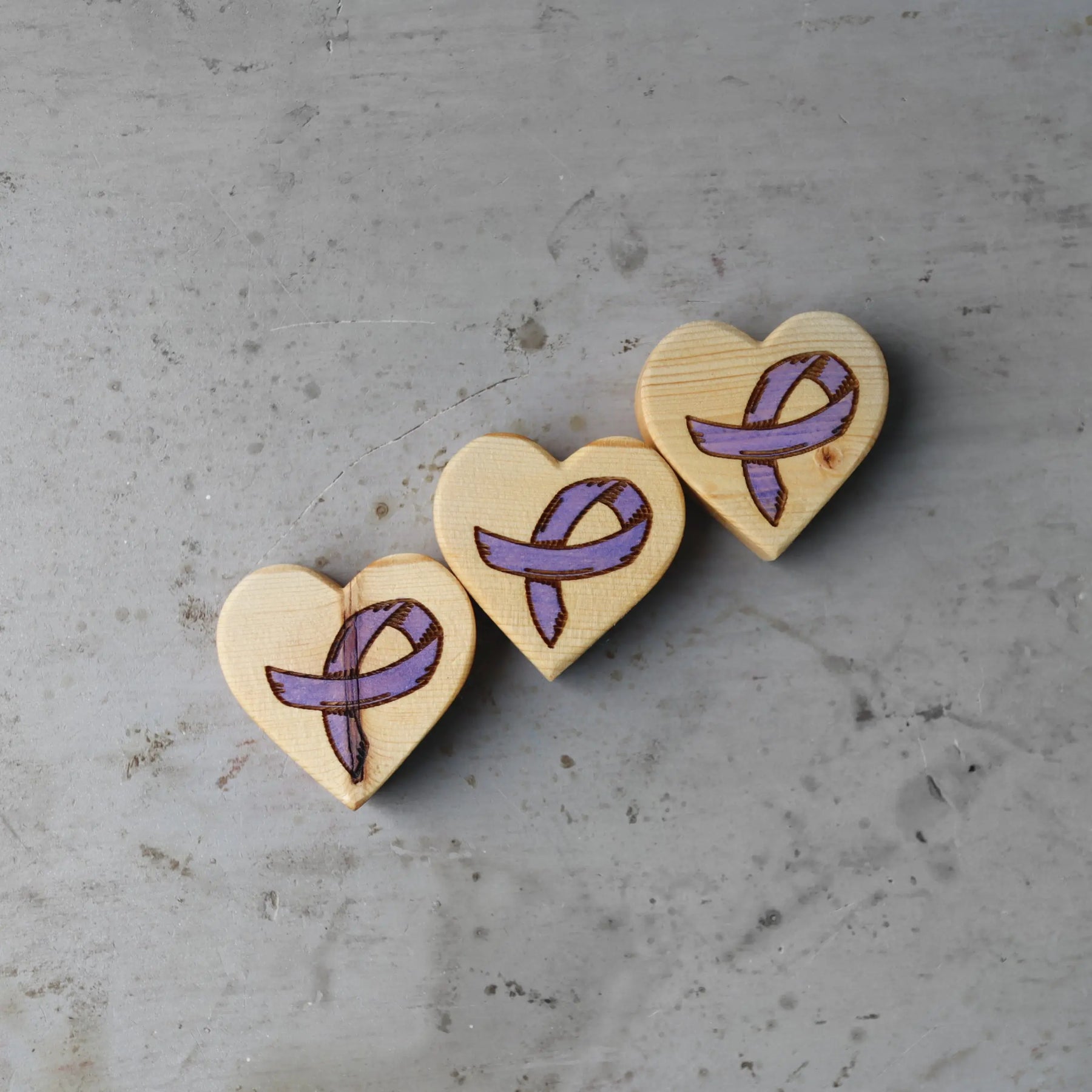 Wooden hearts with engraved purple ribbons for cancer awareness.