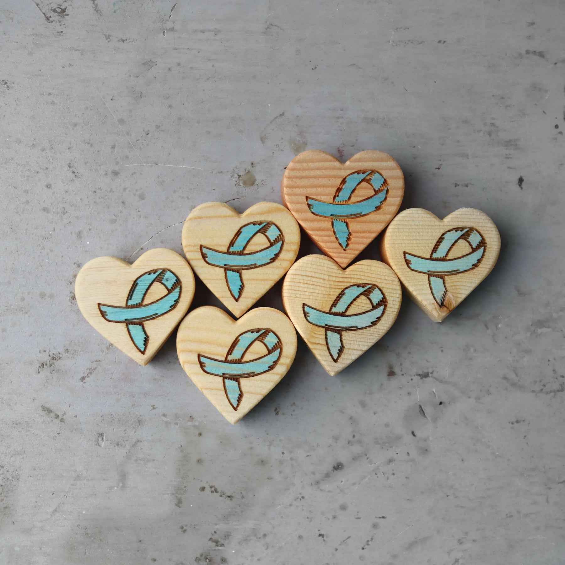 Wooden heart charms with light blue awareness ribbons on gray surface.