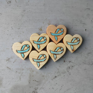 Wooden heart charms with light blue awareness ribbons on gray surface.
