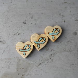 Three wooden hearts with teal ribbon design on textured gray surface.
