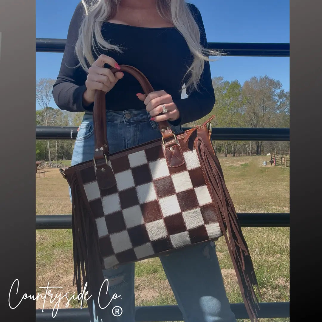 Brown and white checkerboard cowhide purse with fringe detail.